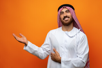 Young Arab man pointing hand to copy space on orange background