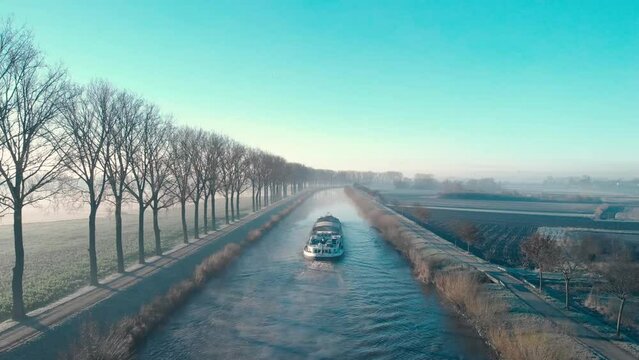 Drone shot dolly forward juste above the water following a barge on the Scheldt river next Escanaffles in the morning with smog and nice light