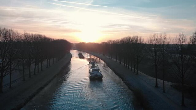 Drone shot dolly forward above two barges crossing on the Scheldt river in the morning with fog and a beautiful golden sunrise on Tournai in Belgium
