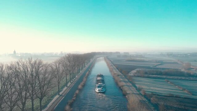 Drone shot dolly forward following a barge on the Scheldt river next Escanaffles in the morning with smog and nice light
