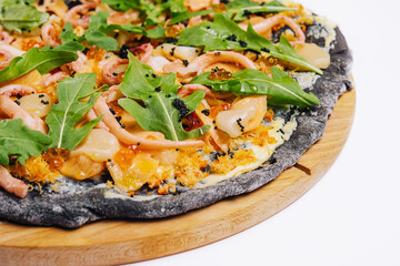 Black pizza with seafood on a wooden round plate on a white
