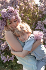 A little stylish boy  with mother  walks among flower trees in spring and mom  holds a kid and hugging outdoor in the nature