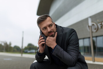 pretty adult man in a business suit talking on a mobile phone while sitting next to a business center