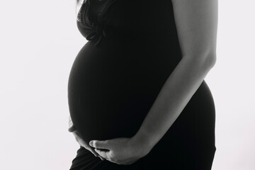 Young adult pregnant woman in white clothes touching big naked belly with hands. Showing shape. Pregnancy concept. Expectation time. Closeup. Isolated on light gray wall background.