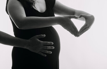 Young adult pregnant woman in white clothes touching big naked belly with hands. Showing shape. Pregnancy concept. Expectation time. Closeup. Isolated on light gray wall background.