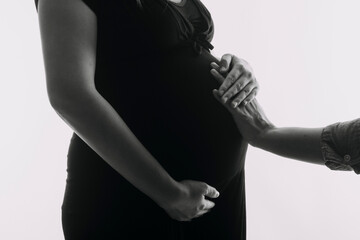 Young adult pregnant woman in white clothes touching big naked belly with hands. Showing shape. Pregnancy concept. Expectation time. Closeup. Isolated on light gray wall background.