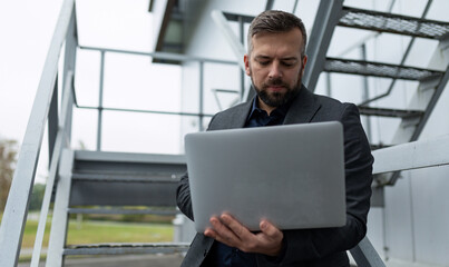 Fototapeta premium adult man in business suit working on laptop online outside