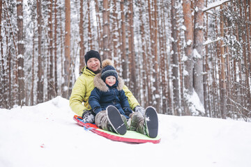 Fototapeta na wymiar Father and little boy sledding and having fun in winter forest. Dad and son spending time together during walking in park.