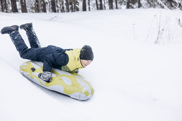 Joyful child boy sledding and having fun. Happy teenager riding on snow tubing in winter forest....
