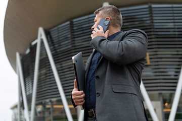 male businessman talking on a mobile phone against the backdrop of an office building, Concept of a successful real estate agent