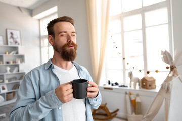 Young bearded man smiling and drinking coffee at home