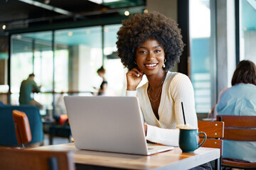 Smiling young african woman sitting with laptop in cafe