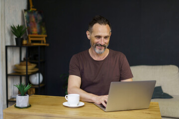 Portrait of middle-age man sitting at his desk in the home office working on laptop and dreanking coffee
