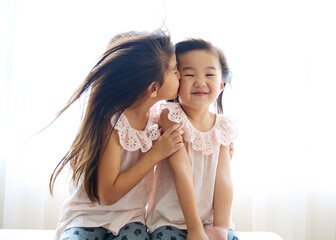 2 asian sisters at home while elder sister kiss on shy younger sister's cheek