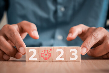 hand is putting wooden cubes with New year 2023 and goal icon. Concept for success in the future goal and passing time. Happy new year.