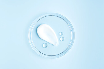 smear of cream stroke and round transparent drops of gel serum in a petri dish on a blue...