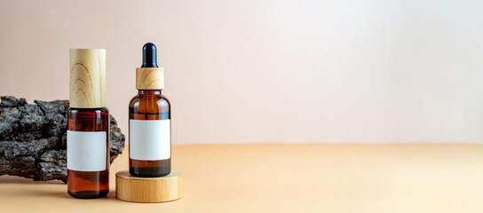 A mock-up of a brown cosmetics bottles with dispenser and white label and dropper bottle with pipette on wooden podium for cosmetics photography on beige background. Banner