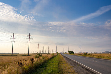 Power lines along the road. Asphalt road and high voltage power towers.