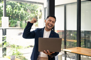 Happy young businessman in suit looking at laptop excited by good news online, lucky successful...