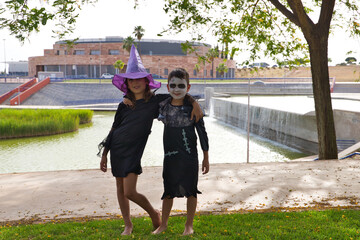 Happy halloween. A girl dressed as a witch with a hat and a boy dressed as a zombie have fun at the halloween party in the park. The children pose for a photo. Trick or treat. 31st October