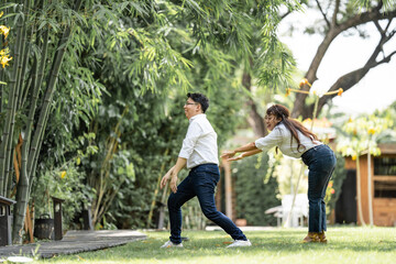 Asian Man and woman taking a pre wedding photo with woman grabbing his shoulder and bracing the man in the garden.
