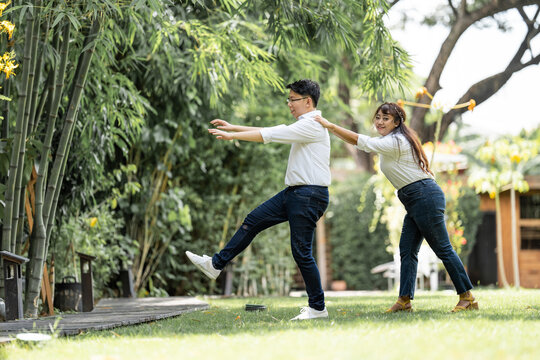 Asian Man and woman taking a pre wedding photo with woman grabbing his shoulder and bracing the man in the garden.