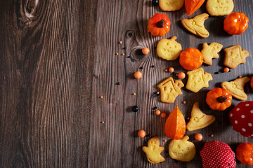 A background of homemade Halloween cookies in the form of a ghost, a witch's hat, a scary house and a pumpkin on a wooden background with fly agarics, a physalis with copy space