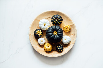 Fototapeta na wymiar Black Gold White Pumpkin For Halloween and Thanksgiving. Minimal Top view flat lay autumn composition with painting black golden trendy pumpkins in round plate