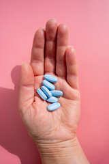 Blue pills in woman hand, vitamins or food supplemets on pink background