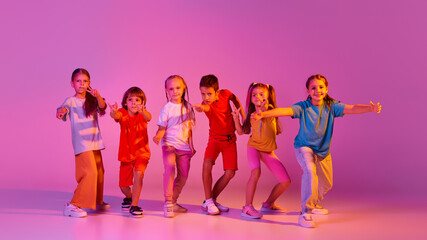 Dance group of happy, active little girls and boys in bright clothes in action isolated on pink...