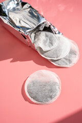 Round tea bag on pink background, sun shadows