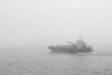 A barge transports a truck across a river. Poor visibility in fog. Passenger and automobile water transportation on a barge. Yana river, Magadan region, Siberia, Far East of Russia. Foggy weather.