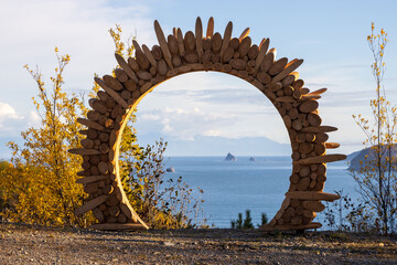 Wooden arch at the observation deck. Sea view. In the distance are rocks in the sea. Ecological tourism and nature travel. Eco trail along the Gertner Bay. Sea of Okhotsk, Magadan region, Russia.