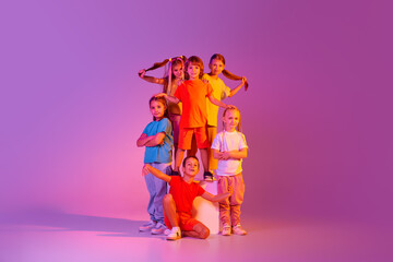 Happy, joyful kids, school age girls and boys in bright clothes posing isolated on pink background in neon. Concept of music, fashion, art, childhood