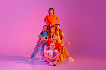 Happy, joyful kids, school age girls and boys in bright clothes posing isolated on pink background in neon. Concept of music, fashion, art, childhood