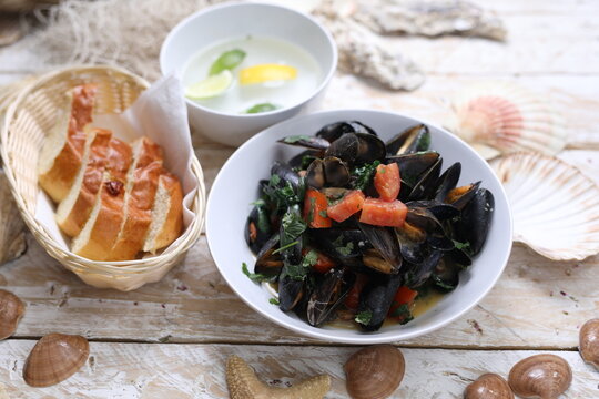Mussels with tomatoes, served with bread, top view. Clams in a bowl, on white wood background.
