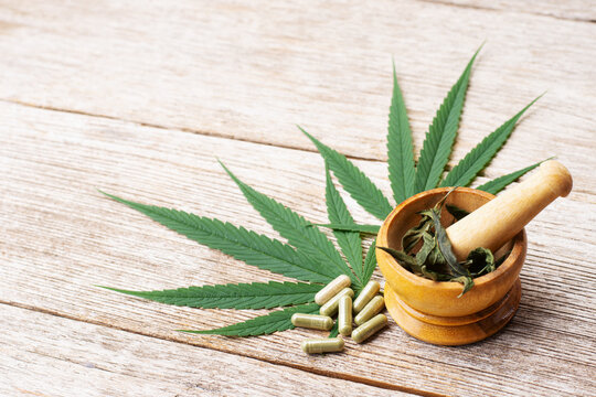 Cannabis leaves and cbd powder capsules pill isolated on wooden table background. 