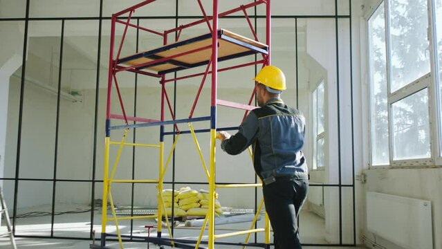 constructor worker rolling the aluminium mobile ladder through the construction site he wearing protective helmet and uniform