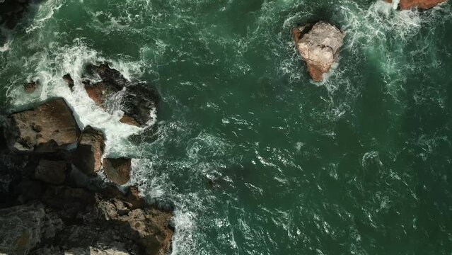 aerial drone top down ocean seascape with waves crashing in to the rock coastline 