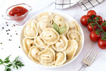 Russian dumplings, dumplings with meat, sour cream, ketchup, tomatoes, bay leaf on a white background. Ukrainian, Russian, Belarusian cuisine.