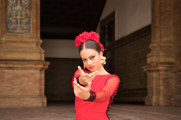 Portrait of young teenage woman in red dance suit with ruffles and red carnations in her hair doing...