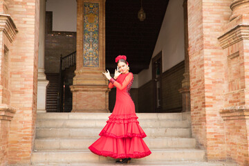 Young teenage woman in red dance suit with ruffles and red carnations in her hair doing flamenco...