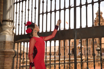 Young teenage woman in red dance suit with ruffles and red carnations in her hair doing flamenco...