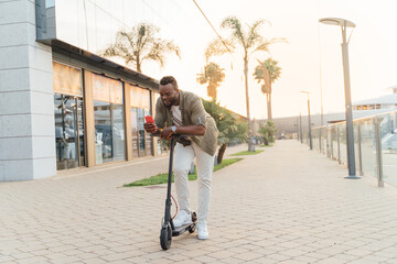 Young african man using a mobile phone on an electric scooter in the street during sunset