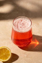 Red cocktail drink with fresh lemon, neutral background, sun light and shadows