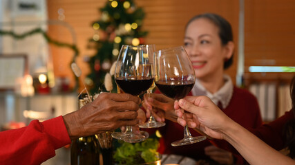 Family toasting wine at Christmas dinner, focus on hands and wine glasses. Holidays and celebration concept 