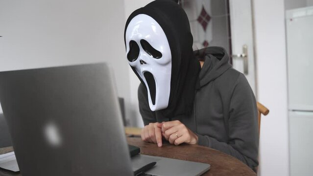 Anonymus person with ghost mask working with laptop. Halloween work concept