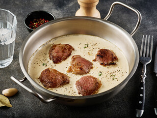 Pork meat medallions with cream sauce in skillet