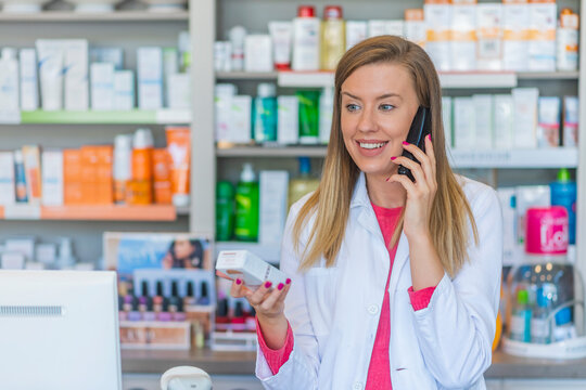 Beautiful young female pharmacist talking on the phone. Pharmacist using landline phone in store. Woman working in a drugstore. Medicine, pharmacy, people, health care and pharmacology concept