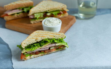 Fototapeta Sandwiches with ham, cheese, tomatoes, cucumbers, lettuce. Sandwiches on a wooden board with sauce in a bowl. obraz